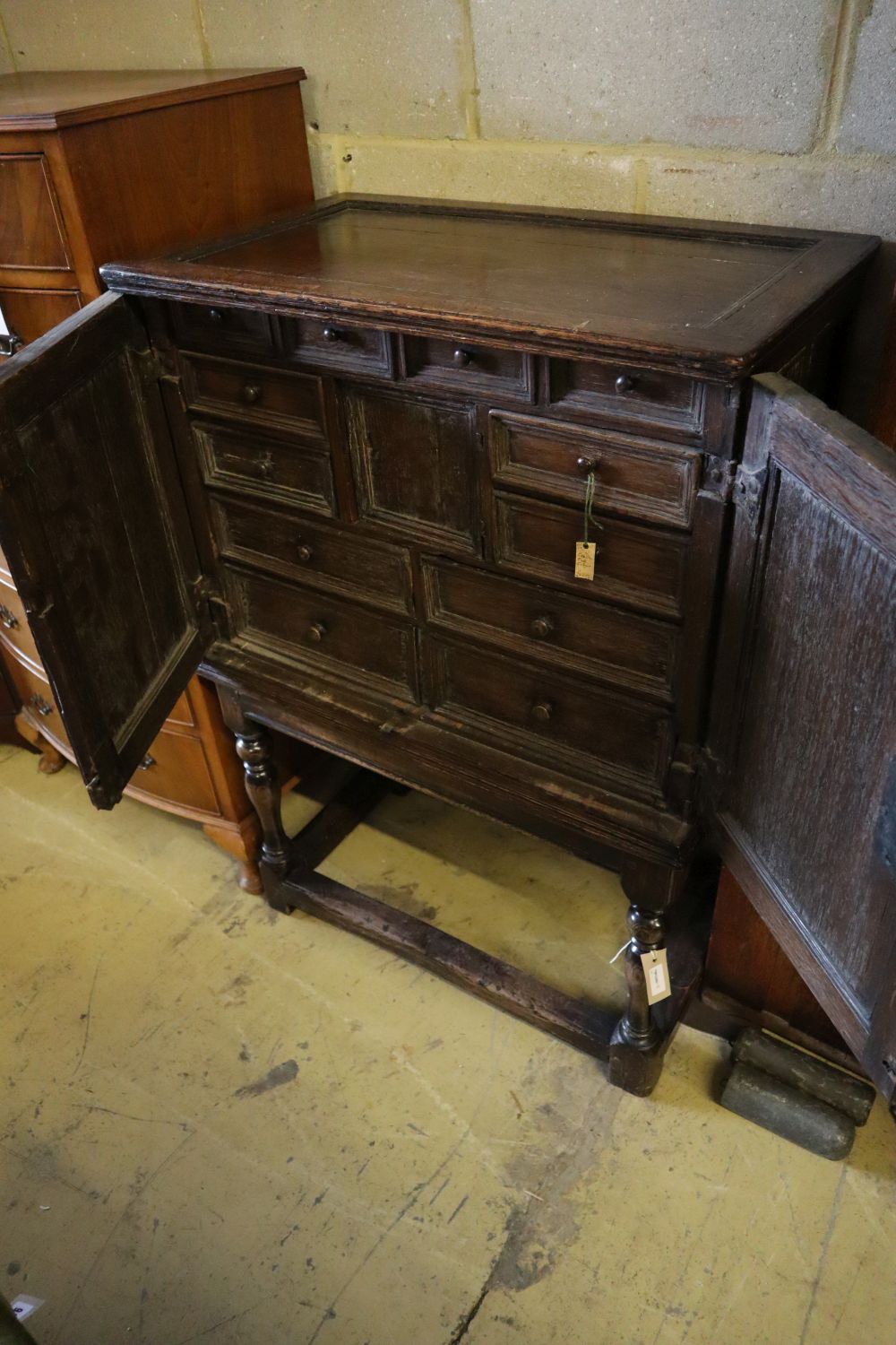 A 17th century and later oak cabinet of drawers enclosed by a pair of panelled doors, with retailers plaque, width 74cm depth 44cm hei